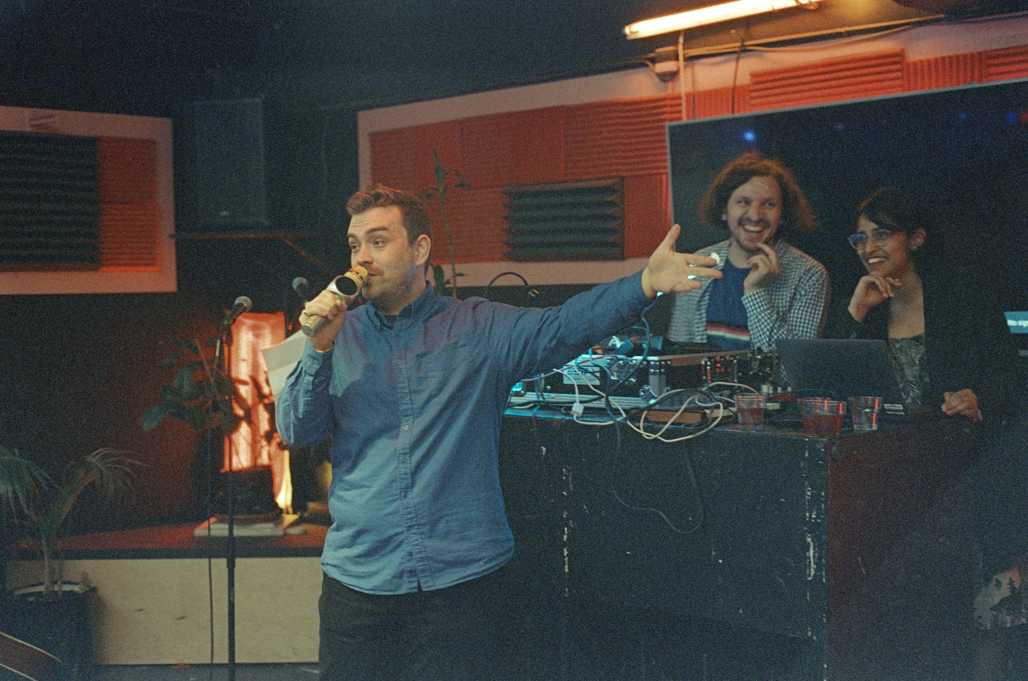 Nikolai makes a toast; Vlad and Fahmia laugh behind the DJ table